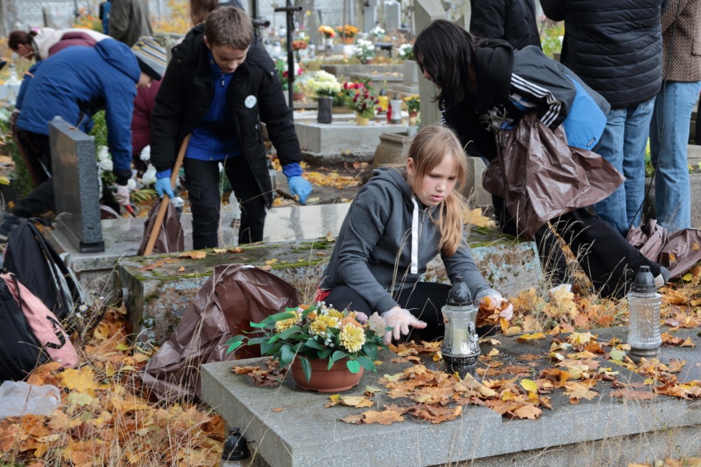 uczniowie odgarniają liście z nagrobków