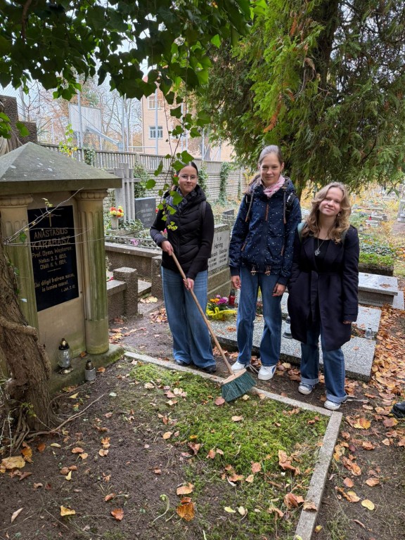 uczennice grabią liście przy nagrobku na cmentarzu