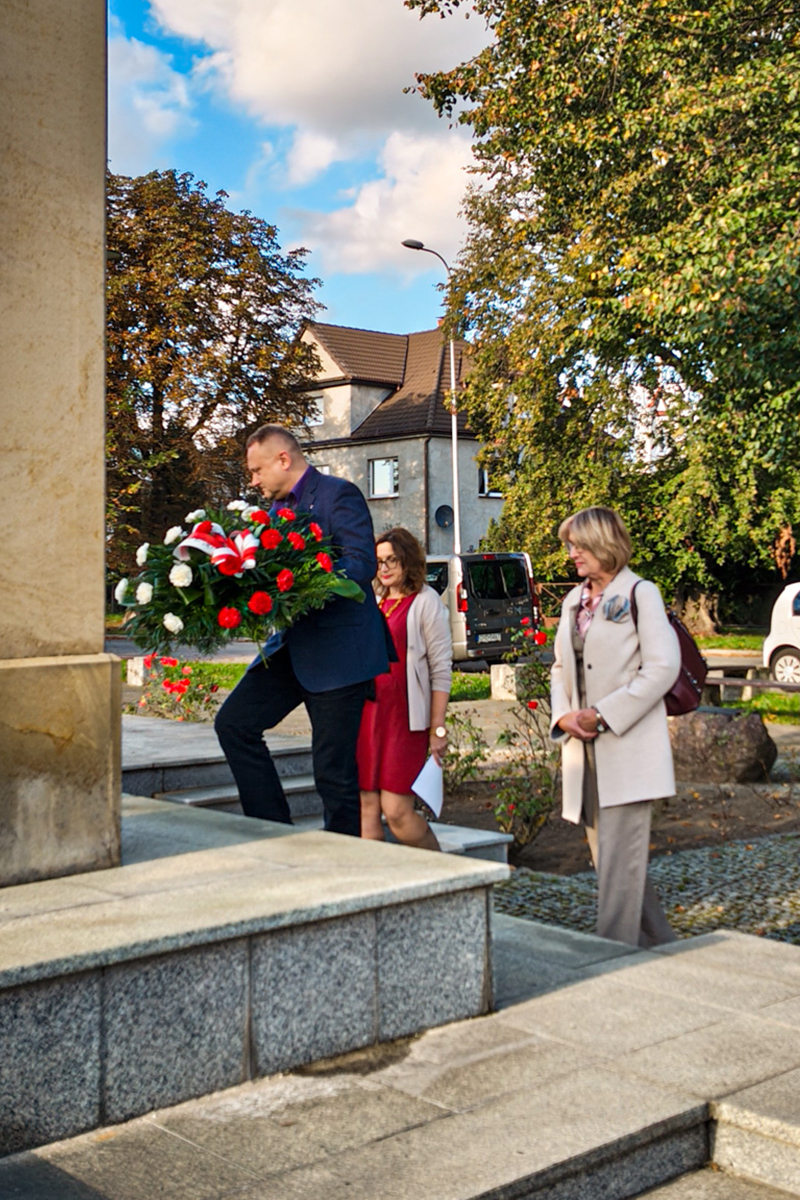 dwie kobiety i mężczyzna podchodzą z wieńcem do bramy piaśnickiej
