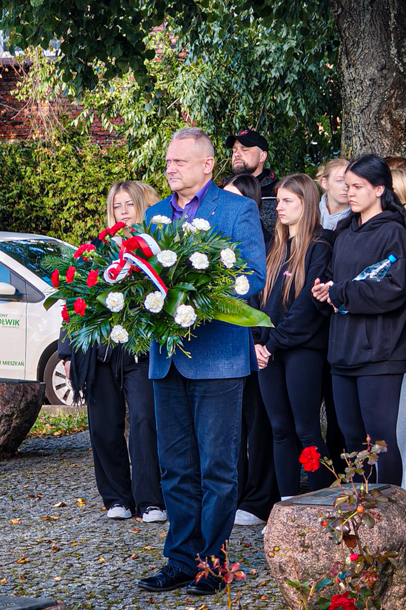 pan stoi z wieńcem za nim grupa młodzieży