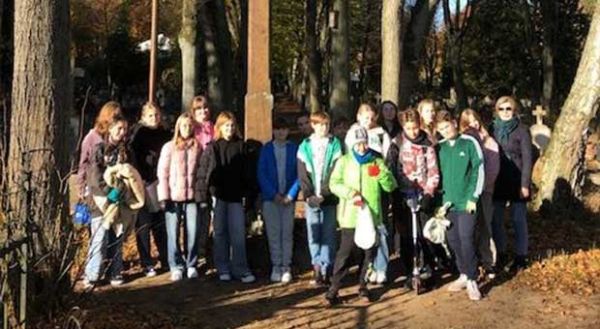 grupa uczniów pozuje do zdjęcia przed krzyżem na cmentarzu