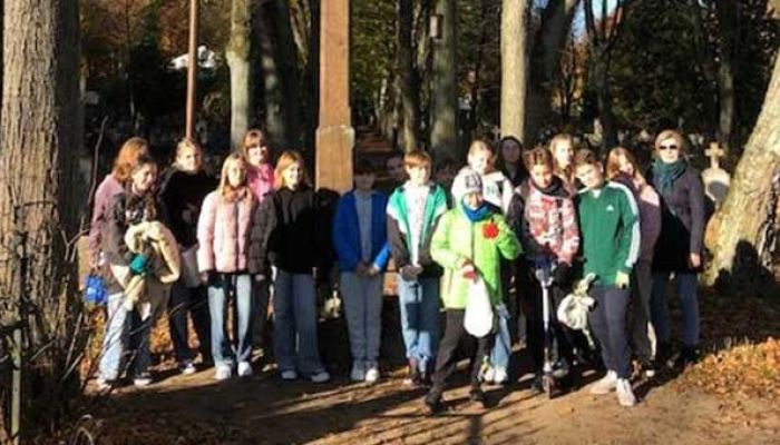 grupa uczniów pozuje do zdjęcia przed krzyżem na cmentarzu