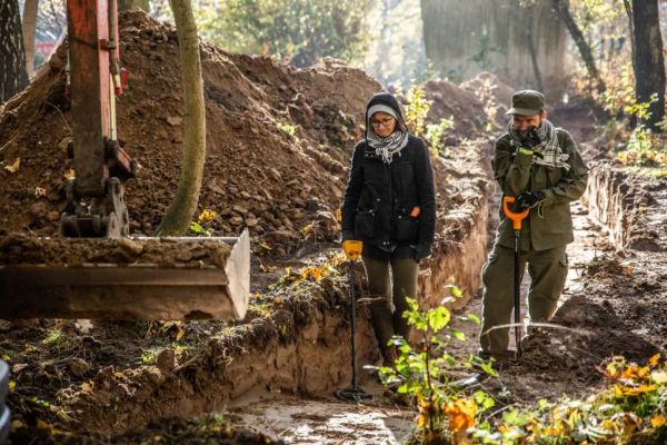 dwóch badaczy kobieta i mężczyzna stoją nad odkrytym grobem masowym